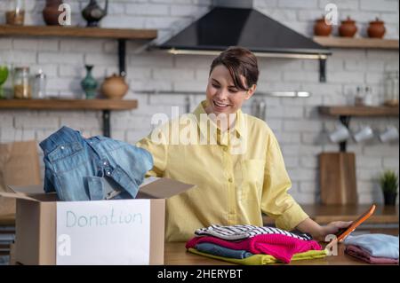 Fröhlicher Vlogger, der Kleidung zur Spende vor der Kamera verpackt Stockfoto