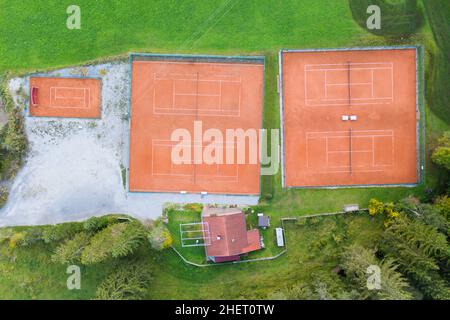 Blick aus der Vogelperspektive auf vier orangefarbene Tennisplätze in grüner Wiesenlandschaft Stockfoto