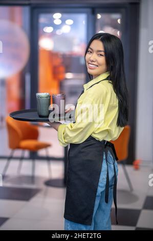 Junge asiatische Kellnerin mit einem Tablett in den Händen Stockfoto