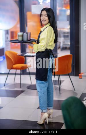 Junge asiatische Kellnerin mit einem Tablett in den Händen Stockfoto