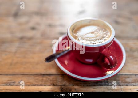 Hochwinkel-Tasse frischen Kaffee mit cremigem Schaum auf der Untertasse neben dem Löffel auf dem Holztisch in der Cafeteria platziert Stockfoto