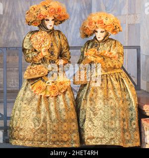 Zwei Frauen in wunderschönen goldfarbenen historischen venezianischen Kostümen, Hut und Maske posieren beim Karneval in Venedig, Carnevale di Venezia, Italien Stockfoto