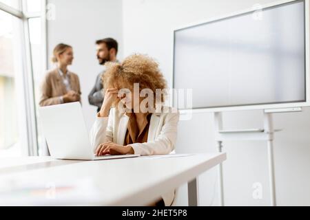 Junge lockige Haare besorgt Geschäftsfrau mit Laptop im Büro mit jungen Menschen arbeitet hinter ihr Stockfoto