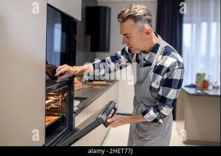 Mann beim Schließen des Backofens, der die Temperaturregelung aktiviert Stockfoto