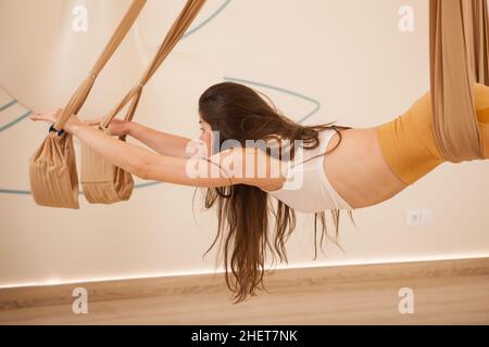 Abgeschnitten Schuss einer langhaarigen fit Frau tun Superman Pose auf Fliege Yoga Hängematte Stockfoto