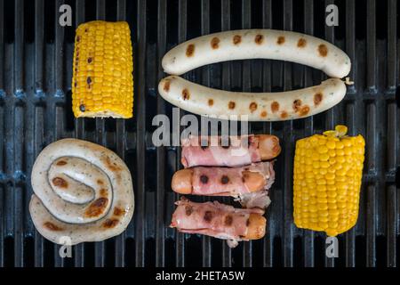 Mais und Würstchen auf schwarzen Eisenstangen des Grills Stockfoto