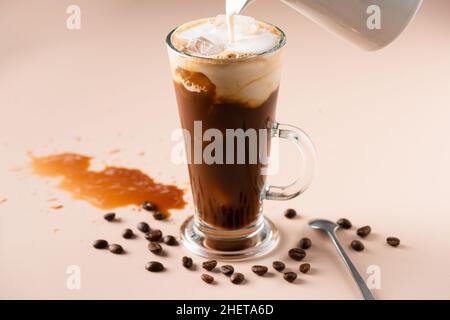 Milch in Eiskaffee gießen, erfrischendes, sommerliches kaltes Kaffeegetränk Stockfoto