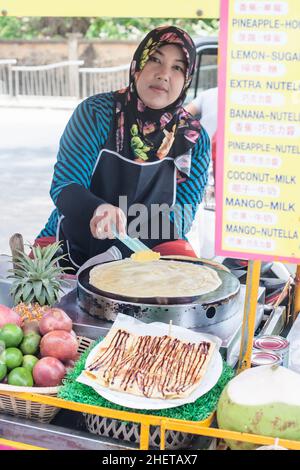 PHUKET, THAILAND - 11. MÄRZ 2018. Ein nicht identifizierter asiatischer Händler bereitet auf der Straße traditionelle süße thailändische Gerichte zu. Pfannkuchen mit Creme. Redaktionelle Tagesaufnahme Stockfoto