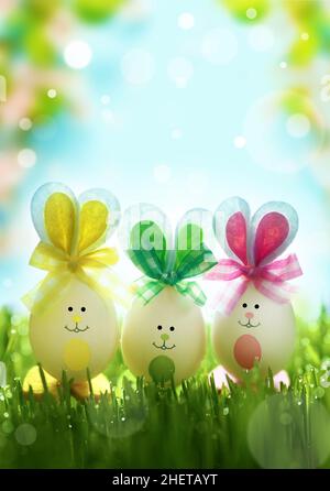 Lustige ostereier im Gras auf blühendem Hintergrund. Frohe Ostern Hintergrund. Osterkompositionen mit niedlichen Kaninchen-Eiern. Osterkonzept. Stockfoto