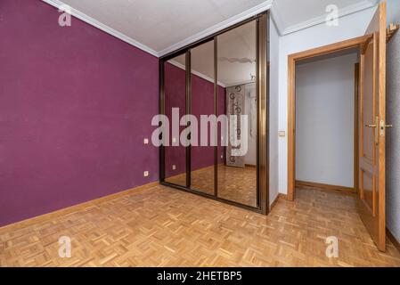 Leeres Zimmer mit violetter Wand und eingebautem Kleiderschrank mit Spiegelschiebetüren Stockfoto