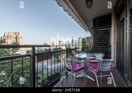 Terrasse mit Markise und Aluminiumtisch und -Stühlen mit Blick auf einen Garten mit Bäumen Stockfoto