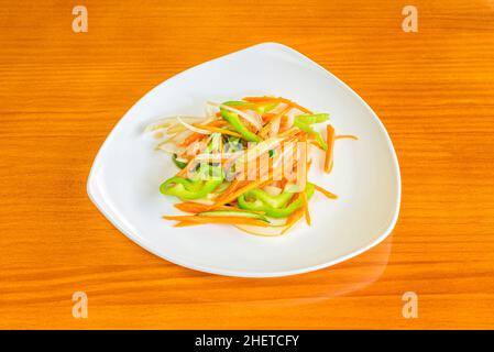 In Streifen geschnittenes Gemüse, das im Wok auf einem weißen Teller gebraten wird Stockfoto