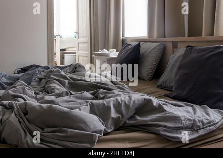 Ein ungemachtes Bett mit zwei Daunendecken in grauer Bettdecke. Morgenkonzept Stockfoto