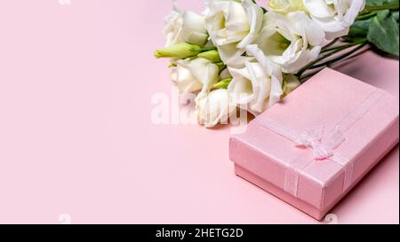 Rosa Geschenkbox und zarte weiße Eustoma-Blumen auf pastellrosa Hintergrund. Geburtstagsgruß, Mutter, Frau oder Valentinstag. Liebe oder Dating-Konzept Stockfoto