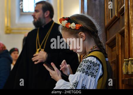 Swjatohirsk, Ukraine. 12th Januar 2022. Ein junges Mädchen im ukrainischen Nationalstil, das während des traditionellen jährlichen Weihnachtsfestes der Weihnachtslieder in Sviatohirsk Lavra (orthodoxes christliches Kloster) mit einem Smartphone gesehen wurde. Die ukrainischen Weihnachtsfeierlichkeiten beginnen am Heiligabend (6. Januar) und enden am Fest der Erscheinung des Herrn. Ukrainische Weihnachtslieder oder Weihnachtslieder haben ihren Ursprung in der Antike, wie viele andere Traditionen, die zur Weihnachtszeit praktiziert werden. Kredit: SOPA Images Limited/Alamy Live Nachrichten Stockfoto