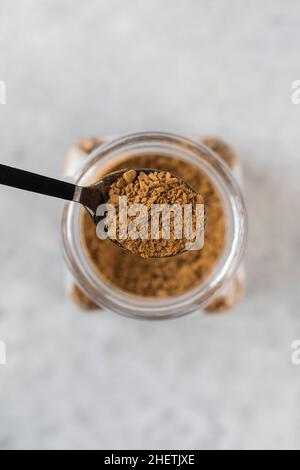 Ein kleiner Löffel mit Instant-Kaffee-Granulat über einem Glas Kaffee. Stockfoto