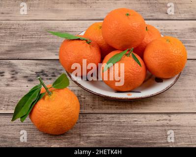 Frische Mandarinen mit Blättern auf einem Holztisch. Reife orangefarbene Mandarinen oder Clementinen auf dem Teller. Gesunder Obstsnack Stockfoto