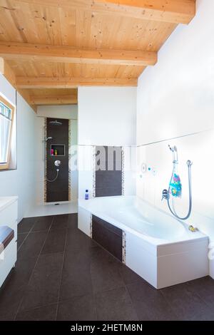 Bad mit Badewanne im Holzhaus und dunkelbraunem Fliesenboden Stockfoto