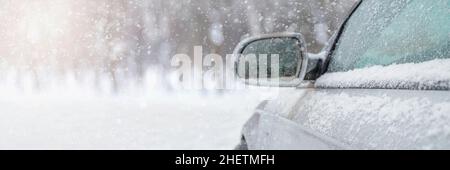 Das Auto fährt durch den Schnee, die helle Wintersonne scheint vor dem Hintergrund des Waldes. Rückspiegel in Nahaufnahme. Das Fahrzeug ist abgedeckt Stockfoto