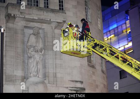 Ein Mann wird auf den Feuerwehrzug gebracht, nachdem er auf die Statuen Prospero und Ariel aus Shakespeares Theaterstück The Tempest des Bildhauers Eric Gill vor dem BBC-Hauptquartier im Zentrum von London geklettert und mit Hammer geschlagen hat. Die Metropolitan Police sagte, dass am Mittwoch gegen 4,15pm Uhr Beamte zum Broadcasting House in der Portland Street, Westminster, gerufen wurden, wo ein Mann eine Leiter benutzt hatte, um die 10 Meter hohen Figuren über dem Vordereingang zu erreichen. Bilddatum: Mittwoch, 12. Januar 2022. Stockfoto