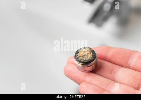 Verschmutzter, verstopfter Belüfter für den Wasserhahn im Bad in der Hand über dem Mixer im Waschbecken. Filter antippen. Wartung von Sanitäranlagen. Calciumschlacke. Wasserhahn Stockfoto