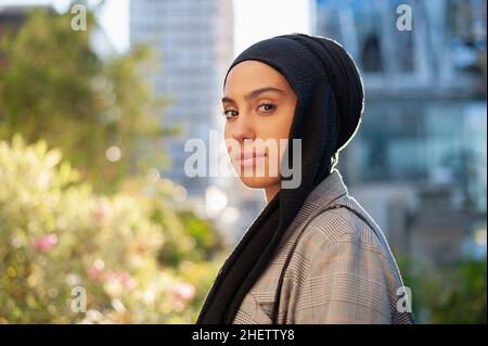 Porträt einer erwachsenen muslimischen Frau mit einem schwarzen Kopftuch, die im Park auf die Kamera schaut Stockfoto
