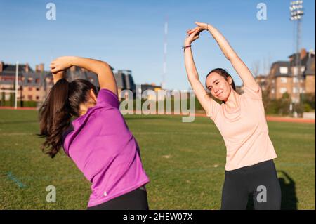 Zwei junge Frauen tun Stretching auf dem Gras eines Laufstrecke vor dem Sport Stockfoto