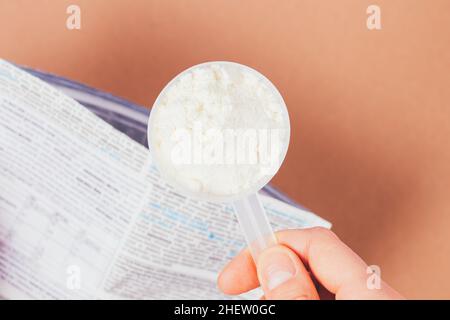Nahaufnahme Schaufel Proteinpulver in der Hand der Frau über offene Packung auf braunem Tisch, Draufsicht Stockfoto