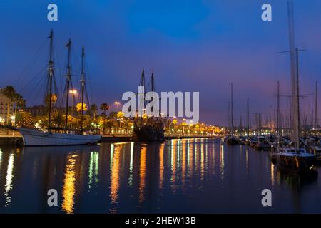 Nachtszene mit einem manipulierten Schoner und hohen Segelschiffen in einem ruhigen Hafen mit farbenfrohen Stadtlichtern von der Uferpromenade, die sich auf der Wasserfront spiegeln Stockfoto