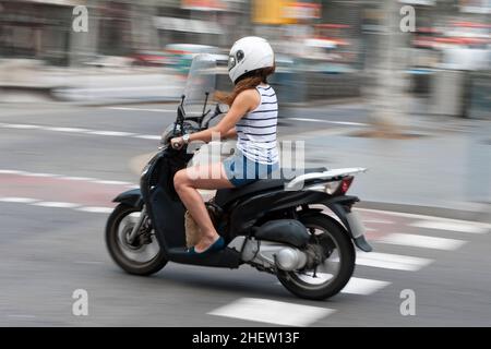 Frau, die in Shorts und Sommertop mit Bewegungsunschärfen auf einem Motorrad eine urbane Straße entlang fährt Stockfoto