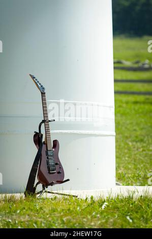 Musikgitarre steht in Träger vor einer großen Stahlsäule mit Gras herum Stockfoto