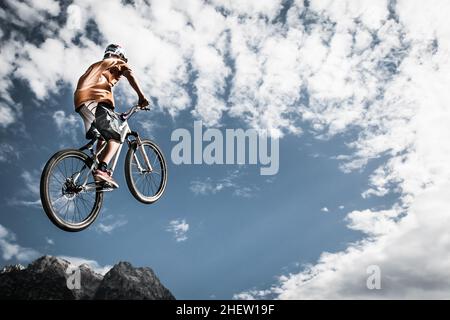 Der Junge springt mit seinem Fahrrad hoch vor Berge und Himmel Stockfoto