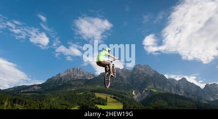 Der junge Freestyler springt mit seinem bmx hoch in die Luft mit schöner Natur, Bergen und bewölktem Himmel im Rücken Stockfoto