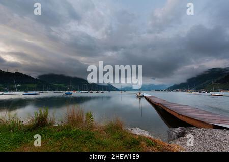 Ein Blick über einen schönen ruhigen See und einen hölzernen Steg mit spiegelruhigem Wasser unter drohenden grauen Wolken, der sich des Sprichwort der ruhigen bef gedanklich darstellt Stockfoto