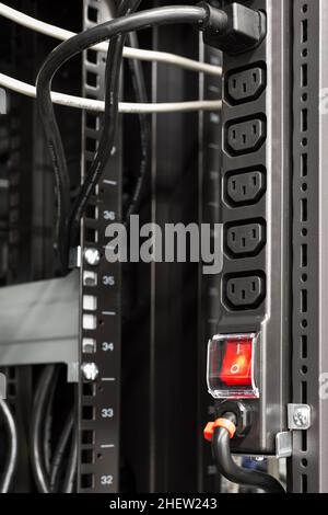 Schwarze Stromleiste im Server-Rack mit roter Hauptschalttaste Stockfoto