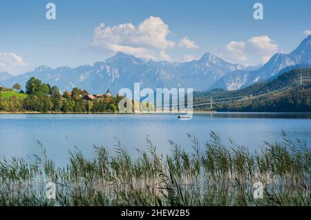 bayerische Landschaft mit See- und Fischerboot und tiroler Bergen und Schilf im Vordergrund Stockfoto