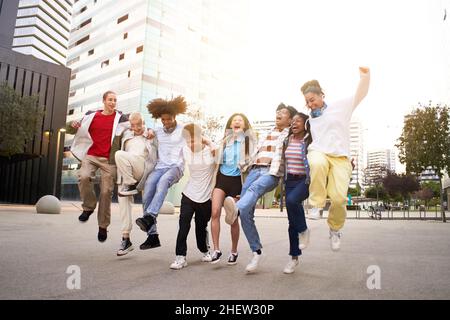 Unbeschwerte glückliche Freunde springen auf der Straße. Eine multiethnische Gruppe junger Teenager, die gemeinsam im Freien Spaß haben. Stockfoto