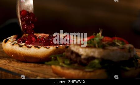 Hausgemachter Grill-Rindfleisch-Burger oder -Sandwich mit Camembert-Käse, Cranberry-Sauce und Beeren, frischem grünem Senfsprossen. Das perfekte Mittagessen der westlichen c Stockfoto