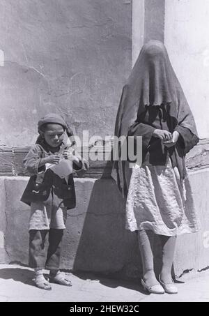 Eine Frau in traditionellem muslimischen Kleid, das ihr Gesicht bedeckt, steht 1988 mit einem Kind in der Altstadt von Kashgar, China. Stockfoto