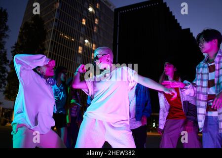 Fahren Sie in Bewegung. Stilvolle Menschen tanzen Hip-Hop in hellen Kleidern auf Stadthintergrund in der Tanzhalle in Neonlicht. Jugendkultur, Bewegung, Stil und Stockfoto