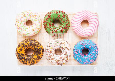 Sechs farbenfrohe glasierte süße Donuts auf einem weißen Holzbrett. Draufsicht, Platz für Text kopieren Stockfoto