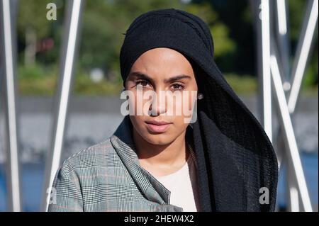 Porträt einer erwachsenen muslimischen Frau mit einem schwarzen Kopftuch, die im Park auf die Kamera schaut Stockfoto