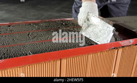 Bauarbeiter mit Kelle zum Nivellieren von Rohmörtel für die Fixierung der Ziegelschichten. Nahaufnahme des Zements, der auf rote Ziegel gelegt wird. Stockfoto