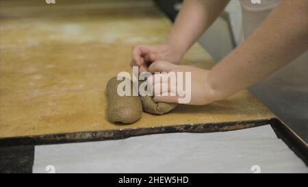 Nahaufnahme für Bäckerhände, die rohes Roggen für das Brotbackkonzept vorbereiten. Frau Hände machen ein Baguette aus dem rohen Roggeteig auf Holzbrett beim Backen Stockfoto