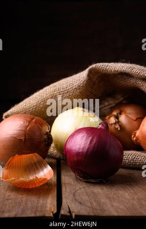 Rote und weiße Zwiebeln auf einem rustikalen Holztisch, die aus einem Stoffsack in der Küche auslaufen, Draufsicht. Hochwertige Fotos Stockfoto