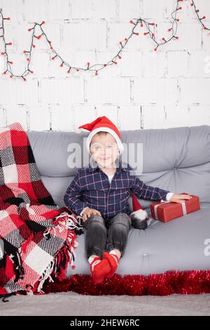 Kleiner Junge in santa hat in der Nähe weihnachten Gnom Spielzeug, halten Zwerg Spielzeug in der Hand in grauen Raum. weihnachtsdekor und Spielzeug. Kinder spielen. Stockfoto