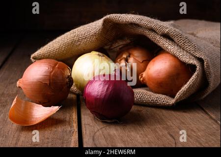 Rote und weiße Zwiebeln auf einem rustikalen Holztisch, die aus einem Stoffsack in der Küche auslaufen, Draufsicht. Hochwertige Fotos Stockfoto