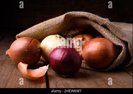 Rote und weiße Zwiebeln auf einem rustikalen Holztisch, die aus einem Stoffsack in der Küche auslaufen, Draufsicht. Hochwertige Fotos Stockfoto