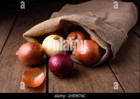 Rote und weiße Zwiebeln auf einem rustikalen Holztisch, die aus einem Stoffsack in der Küche auslaufen, Draufsicht. Hochwertige Fotos Stockfoto