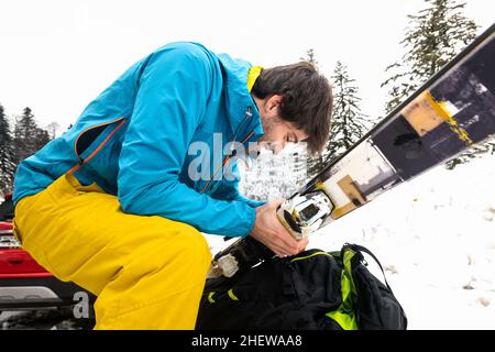 Junger Kaukasischer in kalter Kleidung, der das Ski-Kit in einem verschneiten Wald vorbereitet. Stockfoto